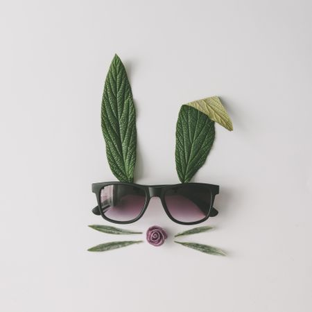 Bunny rabbit face made of natural green leaves with sunglasses on bright background