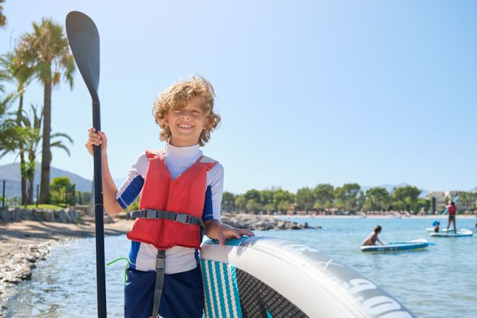 Happy child with paddle and SUP board on seashore