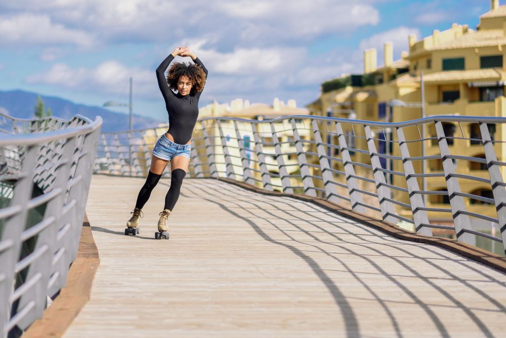Happy woman with afro hairstyle rollerblading on wooden bridge
