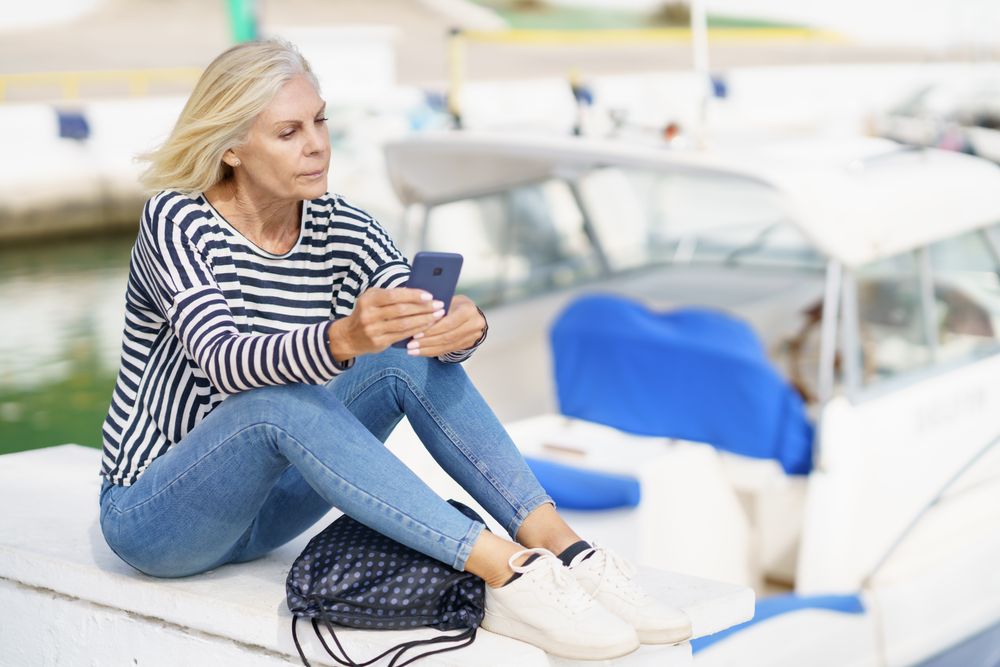 Older woman using her smartphone sitting on the pier