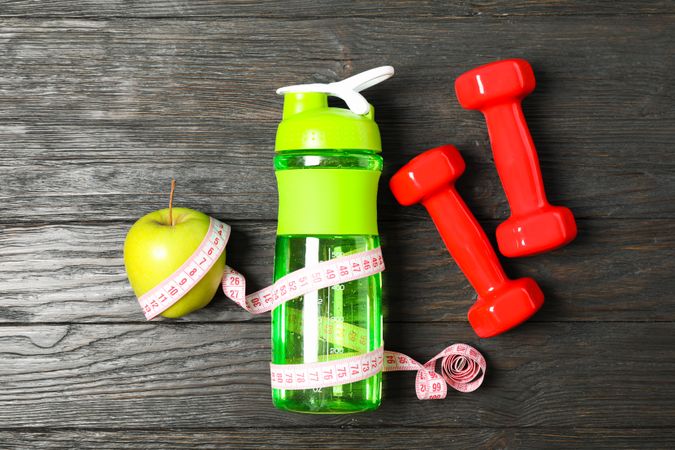 Bottle, measuring tape and apple on wooden background, copy space