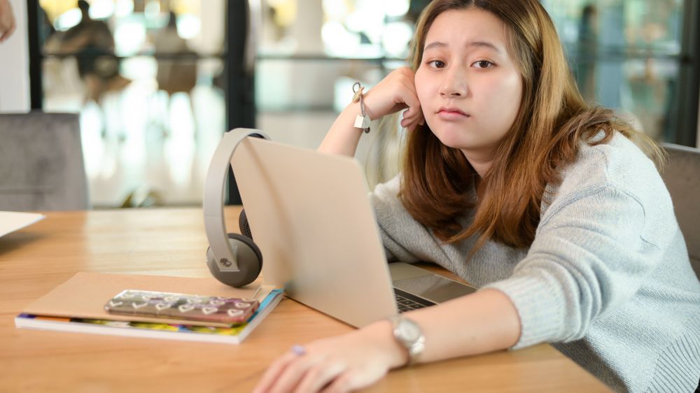 Young Asian woman looking at the camera making a confused face sit back and relax while studying online at home.