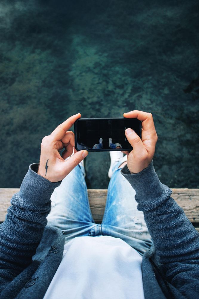 Man sitting on pier taking picture of the water, vertical