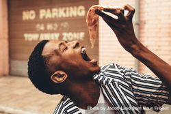 Young man eating pizza slice outdoors bGxqx0
