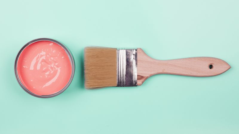Top view of coral paint bucket and paintbrush on mint background