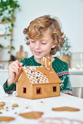 Cheerful boy applying icing on gingerbread house