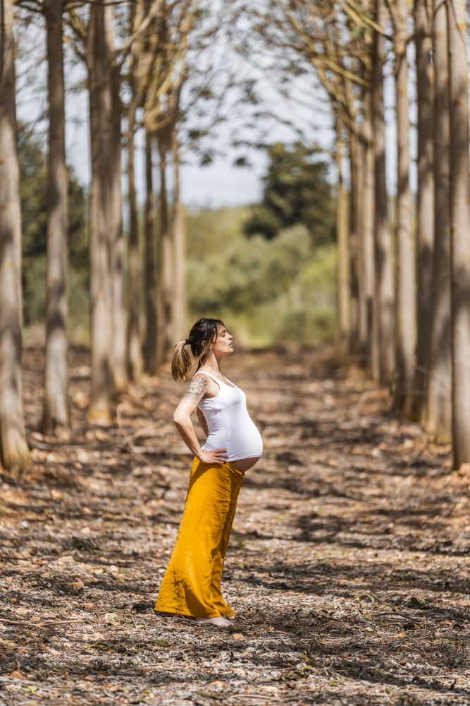 Adult expectant mother practicing yoga in park during sunny day