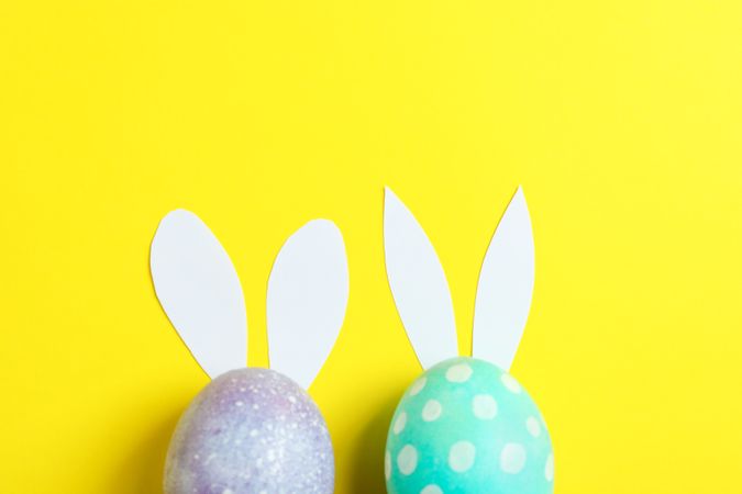 Decorated Easter eggs with cute bunnies ears on yellow background. Space for text