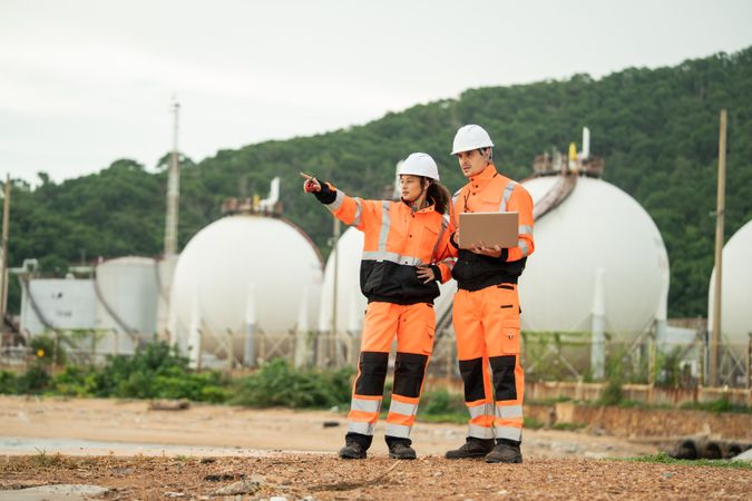 Two engineers in safety gear talking work near spherical gas storage tanks.
