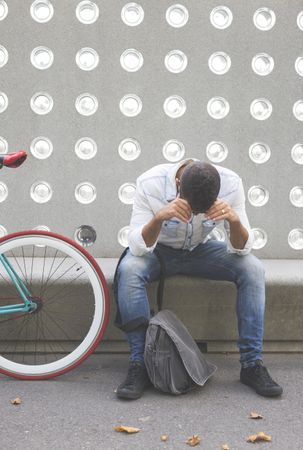 Tired male sitting with bike parked in front of patterned cement wall, vertical