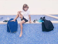 Blond boy with swimming equipment near pool