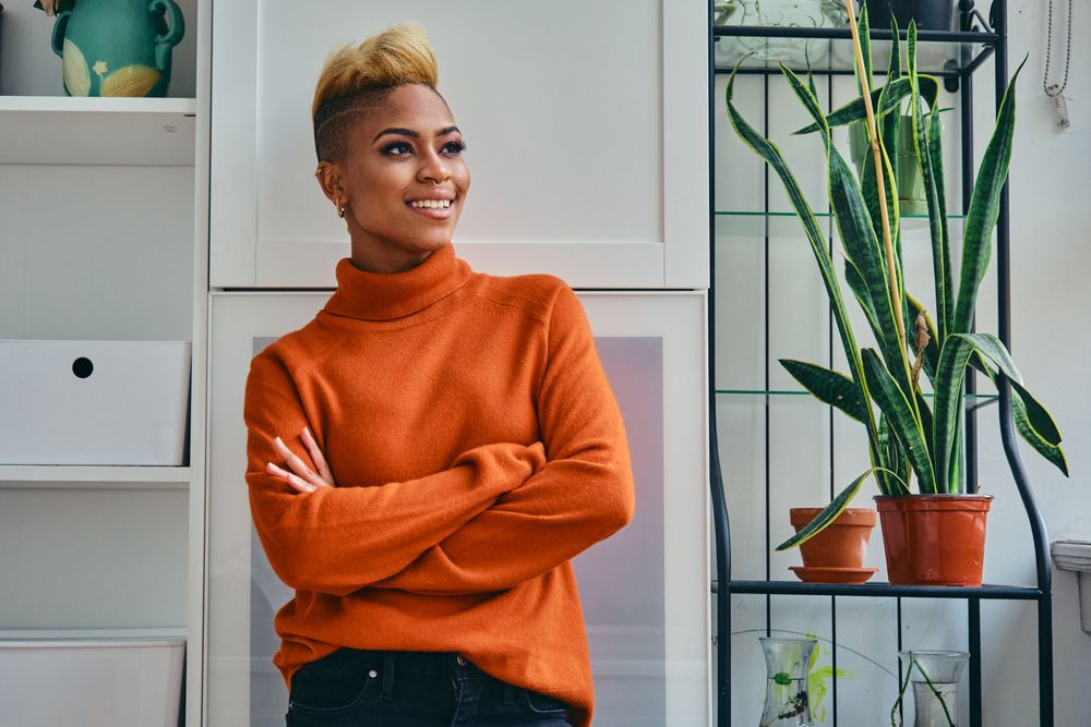 Content Black woman with arms crossed in a bright home with plants