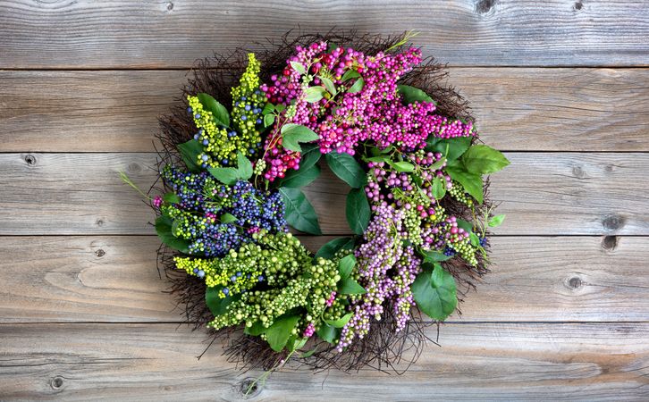 Colorful artificial wreath made of flowers and leaves on vintage wood background