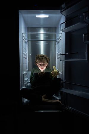 Funny boy with tablet sitting in refrigerator