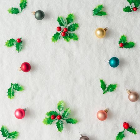 Pattern of plastic holly and baubles on snow background
