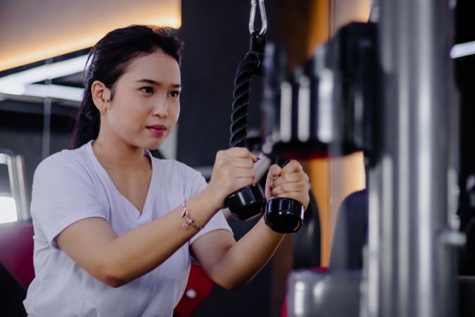 Focused brunette exercising triceps with rope pulldown at the gym