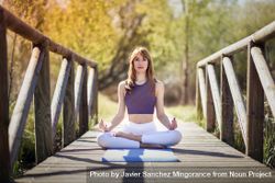Woman wearing sport clothes meditating with eyes closed on yoga mat on forest path bG9ol5
