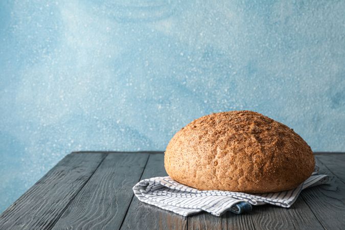 Bread on kitchen towel on wooden table against light background, space for text