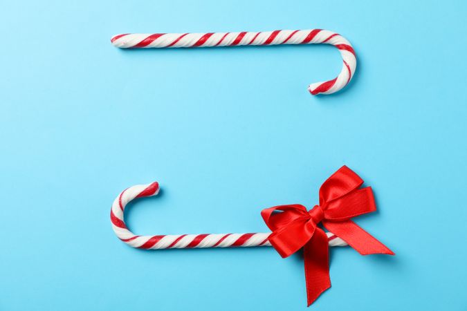 Sweet candy canes and bow on color background, space for text