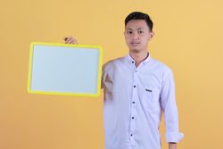Portrait a young man in yellow backdrop holding a blank note board