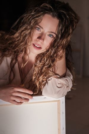 Dreamy young woman with hands on canvas looking at camera