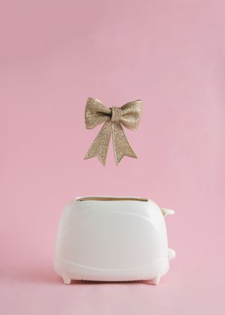 Golden bow popping out of toaster on a soft bright beige background
