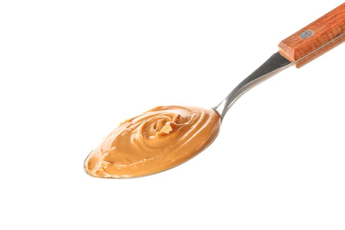 Creamy peanut butter in spoon isolated on light background. A traditional product of American cuisine