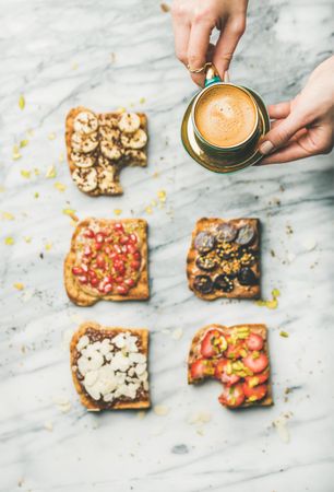 Toast topped with fresh fruit on marble background with woman holding coffee