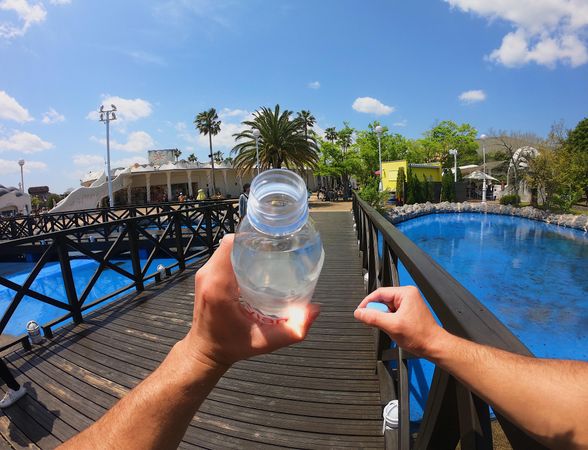 Cropped image of hand holding water bottle near wooden bridge over swimming pool