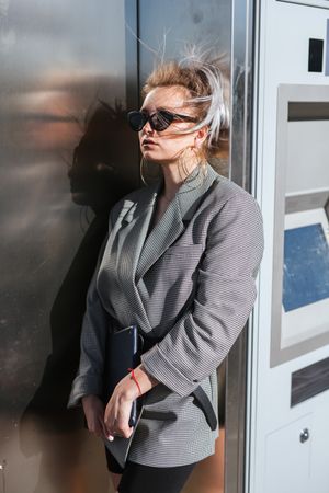 Stylish woman in black sunglasses leaning on metal wall
