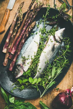 Sea bass with herbs and purple asparagus in dark bowl, vertical composition