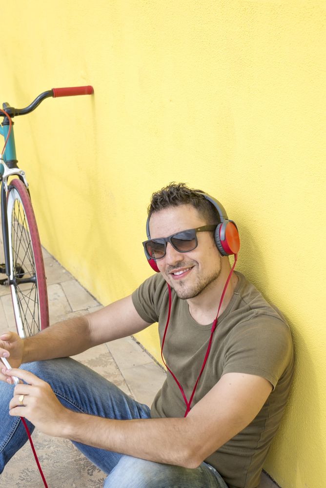 Looking down at smiling man with red headphones sitting outside, vertical