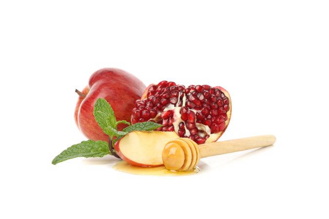 Honey dipper, open pomegranate, mint, and apple centered on plain table