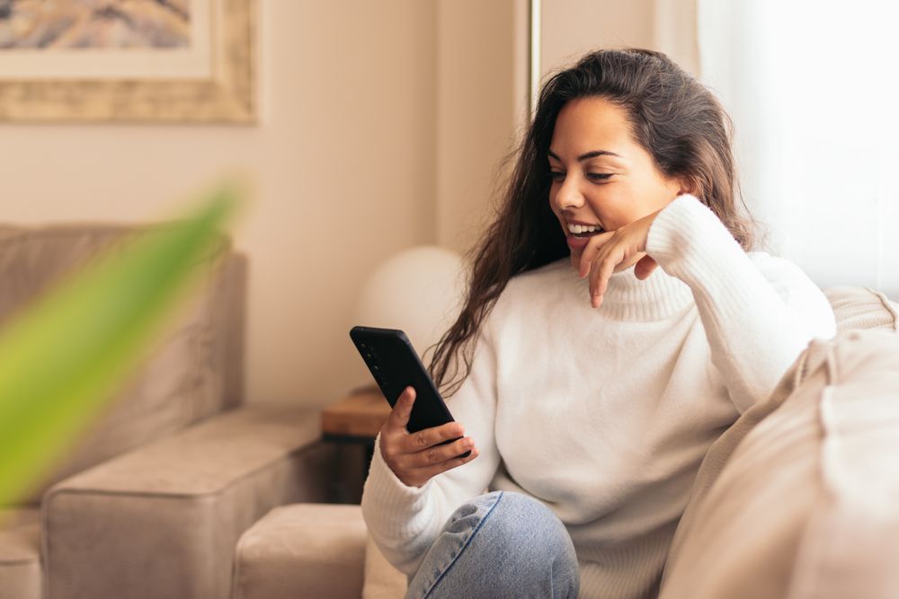 Connected at Home: Young Woman Sitting on Sofa Using Smartphone