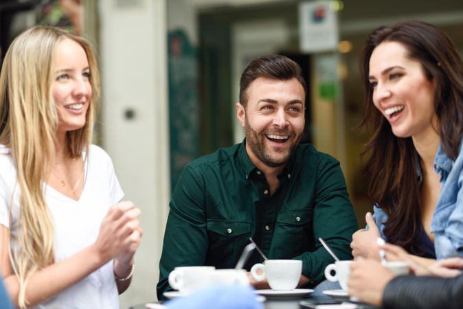 Three friends laughing over coffee outside