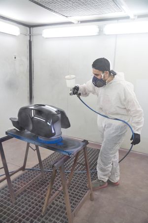 Master in mask painting motorcycle tank on table
