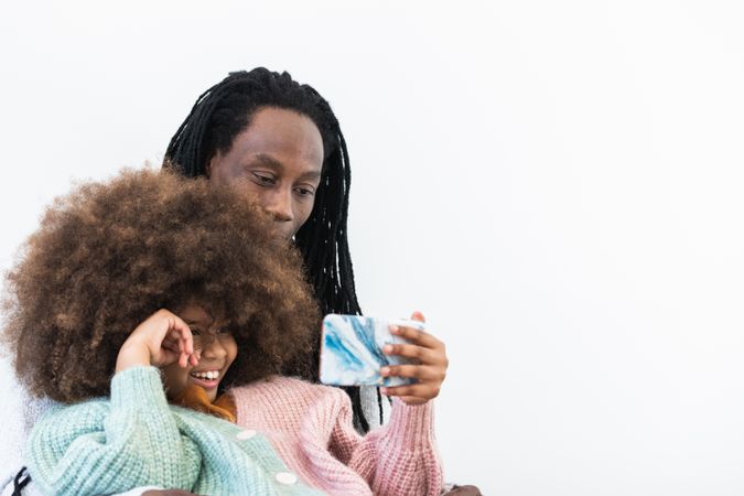 Black man embracing daughter while watching smartphone together