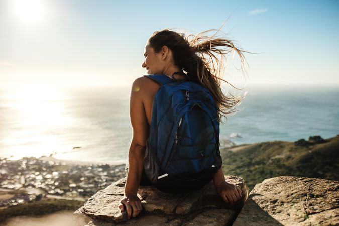 Female hiker relaxing on mountain top facing the ocean