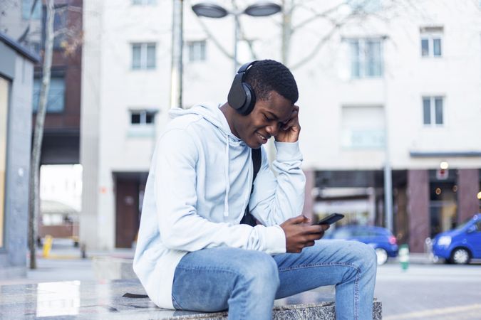 Smiling Black man sitting in the street while listening music on headphones