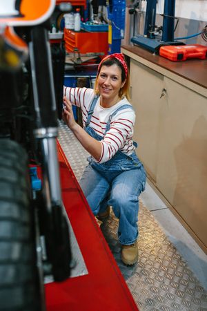 Portrait of mechanic woman repairing motorcycle on factory