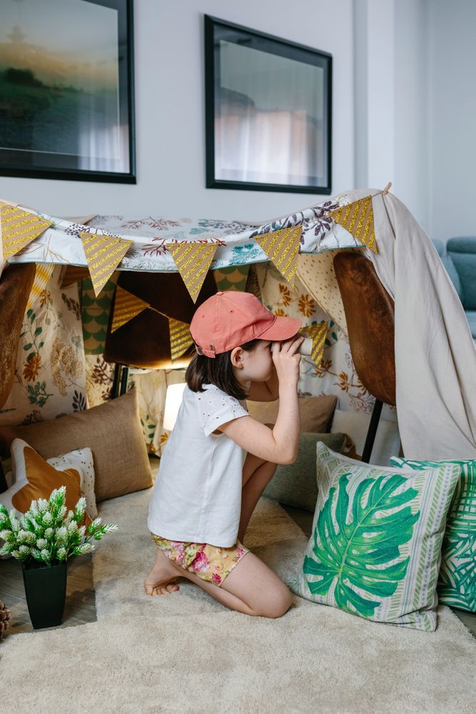 Girl playing with cardboard binoculars while camping at home