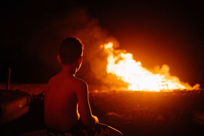 Back of young boy watching fire in field at night