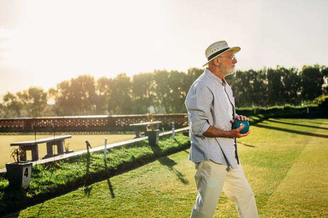 Man in hat playing boules in a lawn with sun flare in the background