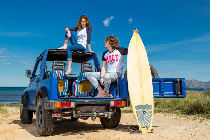 Guy with surfboard and woman on roof of car