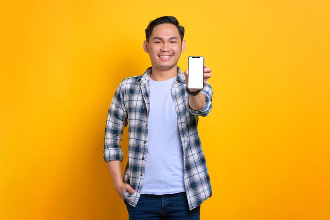 Content Asian male holding up smart phone with blank screen