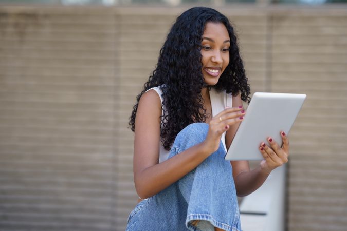 A young woman is engaged with her tablet while sitting outdoors in a vibrant urban setting