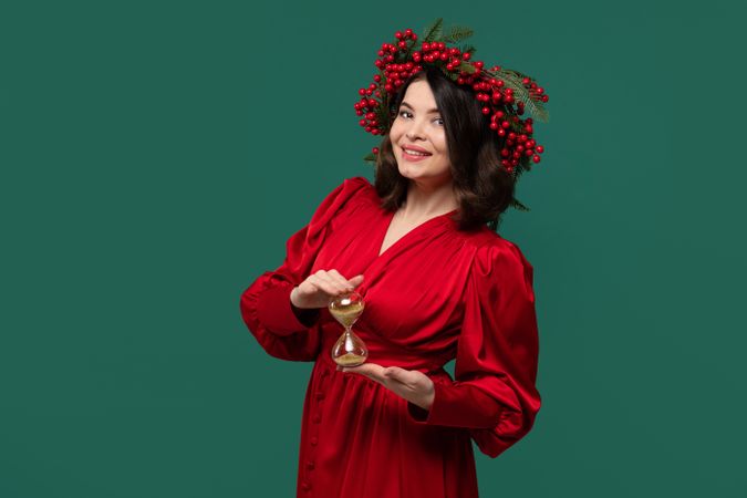Woman in red dress with berry wreath holding hourglass.