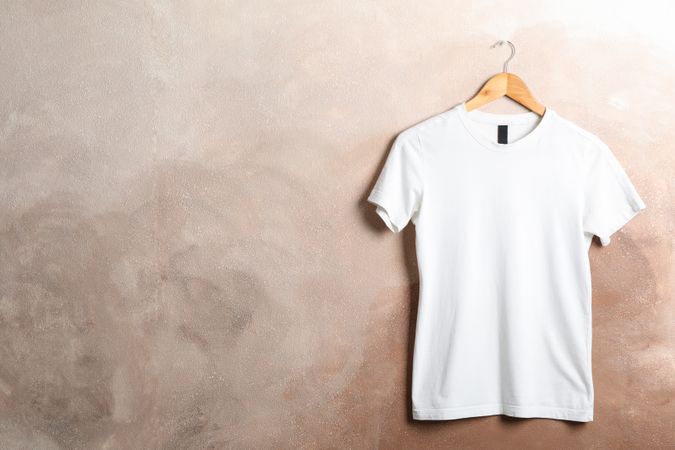 Hanger with blank plain t-shirt on brown background, space for text
