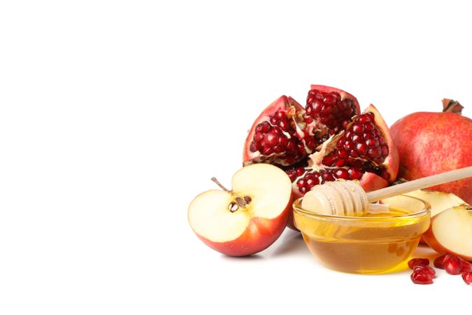 Pot of honey with dipper, open pomegranate and apples on right with copy space