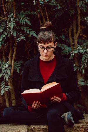 Young woman reading book on bench in park